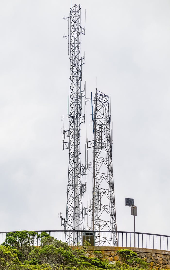 Two tall communication towers on a hill with a cloudy sky.