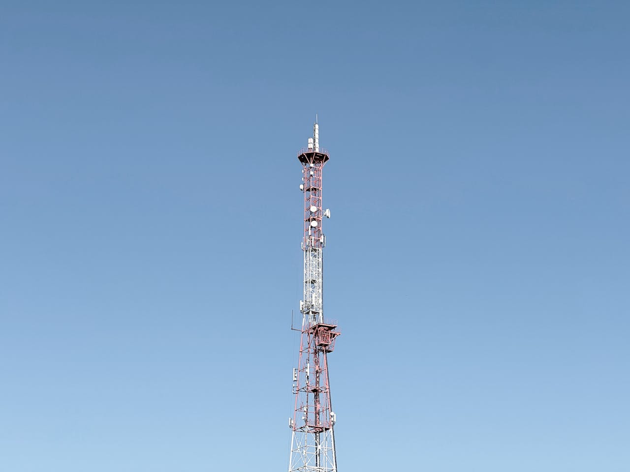 A tall communication tower set against a cloudless blue sky, symbolizing modern telecommunications.